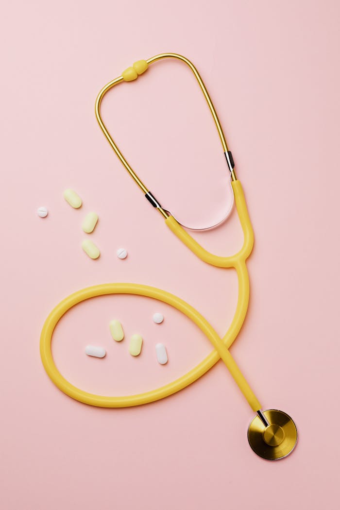 services-02 Flat lay of a yellow stethoscope and assorted pills on a pastel pink background.